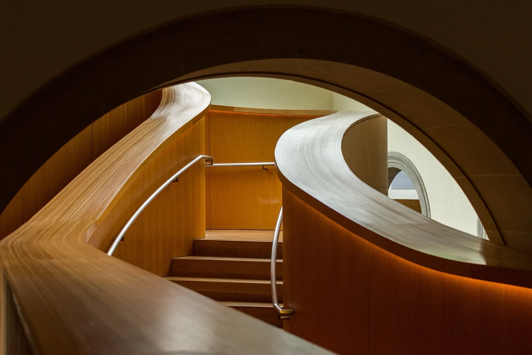 Geschwungener Holzbogen über einer Treppe, von Licht durchflutet