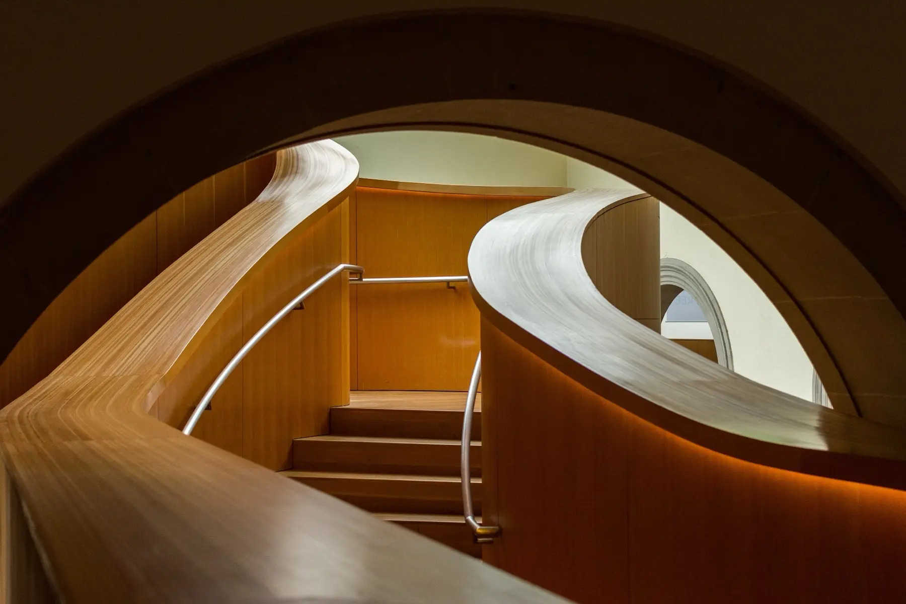 Geschwungener Holzbogen über einer Treppe, von Licht durchflutet